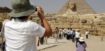 أحد السائحين الأجانب يلتقط صورا لتمثال أبو الهول والأهرامات