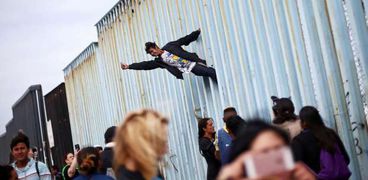 رجل يتسلق الجدار العازل بين المكسيك والولايات المتحدة