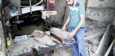 «سنقر» أثناء تجهيزه الأخشاب اللازمة لصناعة عربة كارو داخل الورشة