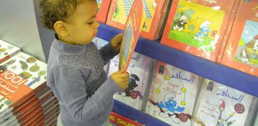 طفلة تمسك بأحد الكتب داخل المعرض