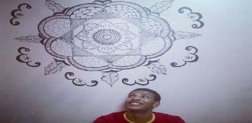 «أحمد» يجلس أمام حائط رسمه بمنزله