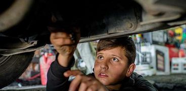 صورة من اليونيسف للاجئ سوري من حلب يعمل تحت سيارة في ورشة لإصلاح السيارات في العراق